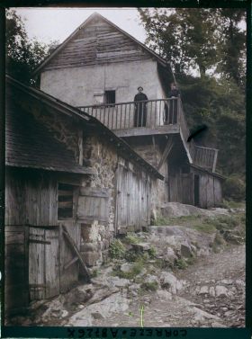 Image représentant Une maison rurale avec loges à cochons au rez de chaussée avec deux femmes au balcon