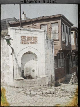 Image représentant Fontaine à l'angle d'une rue et maisons de bois