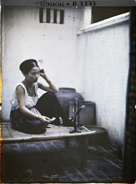 Image représentant Une jeune élégante de classe aisée à sa toilette, assise sur une banquette en bambou dans la cour intérieure de son habitation