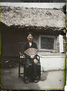 Image représentant La mère de l'un des jeunes époux, assise dans un fauteuil en bois, un éventail déployé à la main, dans une cour intérieure