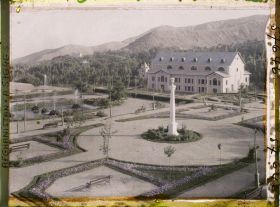 Image représentant Dans le Jardin public (Bâgh-e omumi), vue sur le jardin depuis la terrasse de la maison de thé; le bâtiment est le théâtre de Paghman (sahna-ye tamsil)
