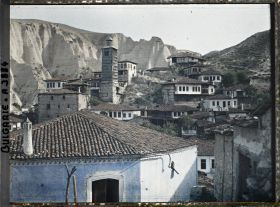 Image représentant Maisons dont une, au premier plan, peinte en bleu, et tour de bois avec à l'arrière-plan les falaises de grès