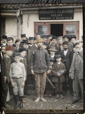Image représentant Jean Brunhes à l'extrême droite et des habitants devant l'enseigne de l'atelier de couture public et militaire du département