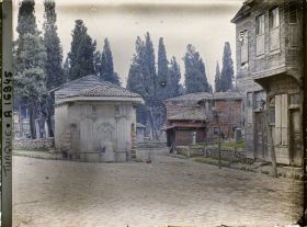 Image représentant Rue pavée, maisons de bois et fontaine devant un cimetière