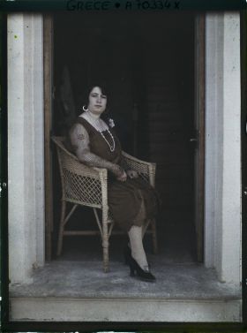 Image représentant Femme d'une quarantaine d'années élégamment vêtue, assise sur seuil d'une maison ou d'un hôtel (guide, interprète, compagne de l'opérateur ?)