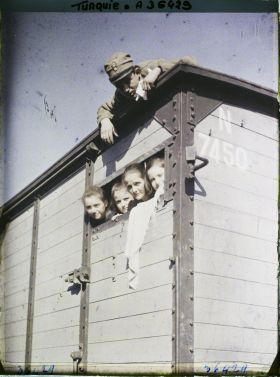 Image représentant Quatre Grecs quittant la ville (une femme et trois enfants) passant la tête dans une ouverture de train de marchandises. Un soldat (grec ou allié ?) sur le toit