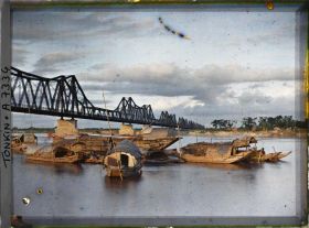 Image représentant Des sampans au soleil couchant sur le Fleuve Rouge devant le pont Doumer