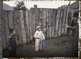 Image représentant Petite fillette en guenilles et en blanc aux pieds pleins de boue. Sur la droite, on peut apercevoir Jean Brunhes lui donnant des instructions