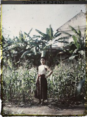 Image représentant Une jeune fille en cache-sein devant un champ de maïs bordé de bananiers