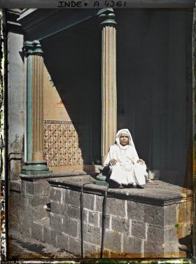 Image représentant Une femme hindoue vêtue de blanc, assise sur la terrasse d'une maison