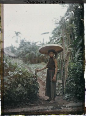 Image représentant Une jeune fille coiffée du grand chapeau en feuilles de latanier, à l'entrée d'un champ