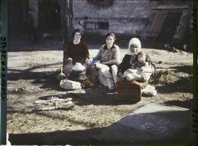 Image représentant Trois femmes grecques dont l'une tenant un enfant, s'apprêtant à quitter la ville, assises aux abords de la gare, près d'un foyer improvisé