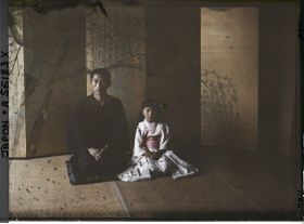 Image représentant Homme et fillette posant devant un paravent de cérémonie