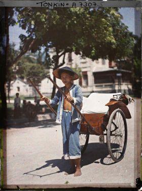 Image représentant Un pousse-pousse à roues caoutchoutées et son tireur, vêtu et coiffé de bleu