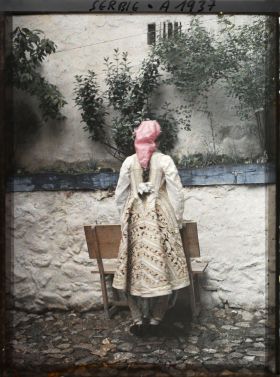 Image représentant Mademoiselle Ljubica, riche costume, foulard de soie rose vif à la tête, vue de dos, manteau brodé d'or
