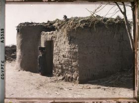 Image représentant Fillette devant une petite habitation en terre séchée aux abords de la capitale