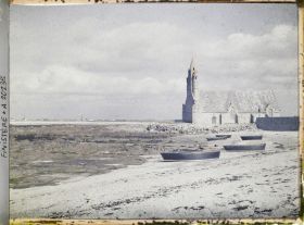 Image représentant Barques échouées sur la grève près de la chapelle Notre-Dame-de-la-Joie. A l'horizon, le village de Saint-Guénolé
