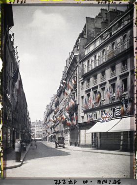 Image représentant La rue des Capucines vue de la rue de la Paix et décorée des drapeaux alliés pour les fêtes de la Victoire des 13 et 14 juillet 1919