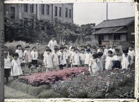 Image représentant Ecole d'Aoyama, jeunes écoliers vêtus à l'occidentale, près d'un massif de fleurs