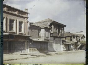 Image représentant Plusieurs maisons dans une rue. A gauche, une maison grecque (panneau en caractères grecs) ?