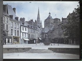 Image représentant La place du Centre avec la fontaine dite "La Plomée" ; à l'arrière-plan, la basilique Notre-Dame-de-Bon-Secours