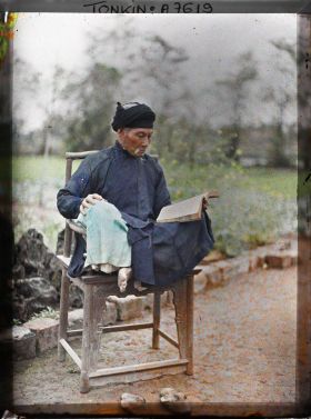 Image représentant Un lettré lisant, assis en tailleur dans un fauteuil en bois