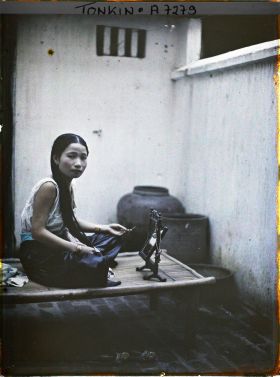 Image représentant Une jeune élégante de classe aisée à sa toilette, assise sur une banquette en bambou dans la cour intérieure de son habitation