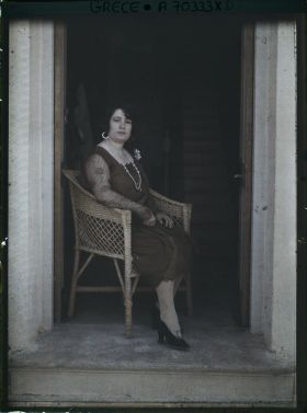 Image représentant Femme d'une quarantaine d'années élégamment vêtue, assise sur seuil d'une maison ou d'un hôtel (guide, interprète, compagne de l'opérateur ?)