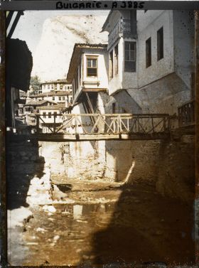 Image représentant Petit pont de bois enjambant une rue de terre battue et bordée de maisons en étages