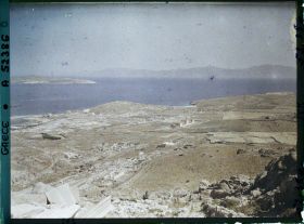 Image représentant Panorama depuis le mont Cynthe en direction du nord-ouest : la ville-haute, puis au bord de la mer, la ville-basse et le port. Au fond, les îles de Syros et plus loin Tinos