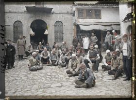 Image représentant Groupe de portefaix tziganes assis devant d'autres habitants et soldats