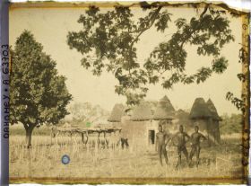 Image représentant Trois hommes somba devant un tata (case) et une plate-forme à sécher le mil