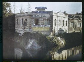 Image représentant France, Verdun, Un garage d'automobiles s/ les bords de la Meuse : On lit l'affiche des Voyges s/ le front.