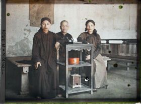 Image représentant Une bonzesse et deux novices assises près d'une desserte supportant un service à thé