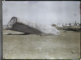 Image représentant Le plus gros des quatre morceaux du Grand Menhir brisé ; à l'arrière-plan, le village de Locmariaquer