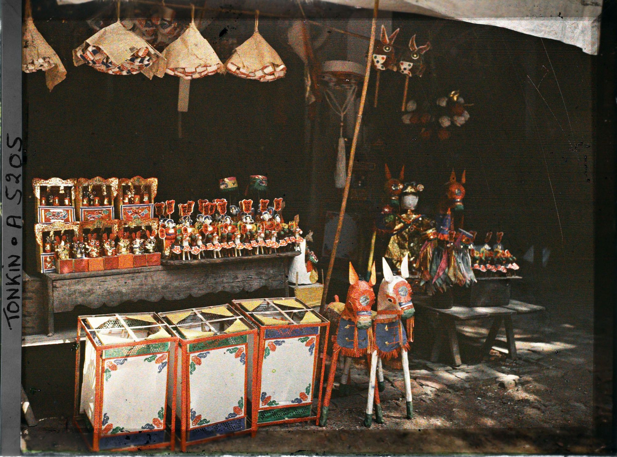 Image représentant Un étalage d'objets votifs et / ou de jouets (?) devant une boutique dans le quartier sino-annamite (?)