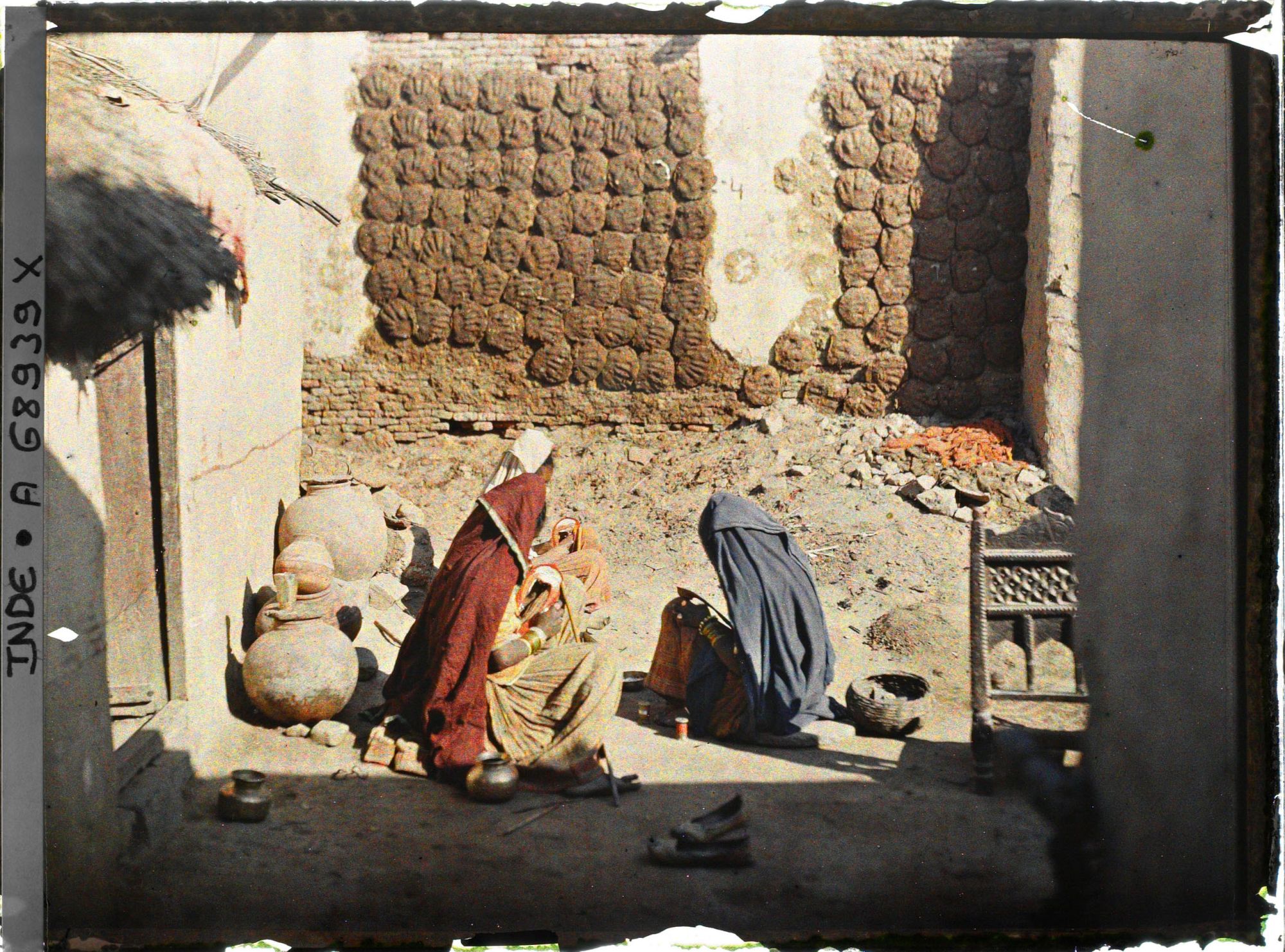Image représentant Séchage des galettes de bouse de vache (utilisées comme combustible en raison de la rareté du bois) dans la cour d'une maison ; au premier plan, groupe de femmes fabriquant des chaussures.