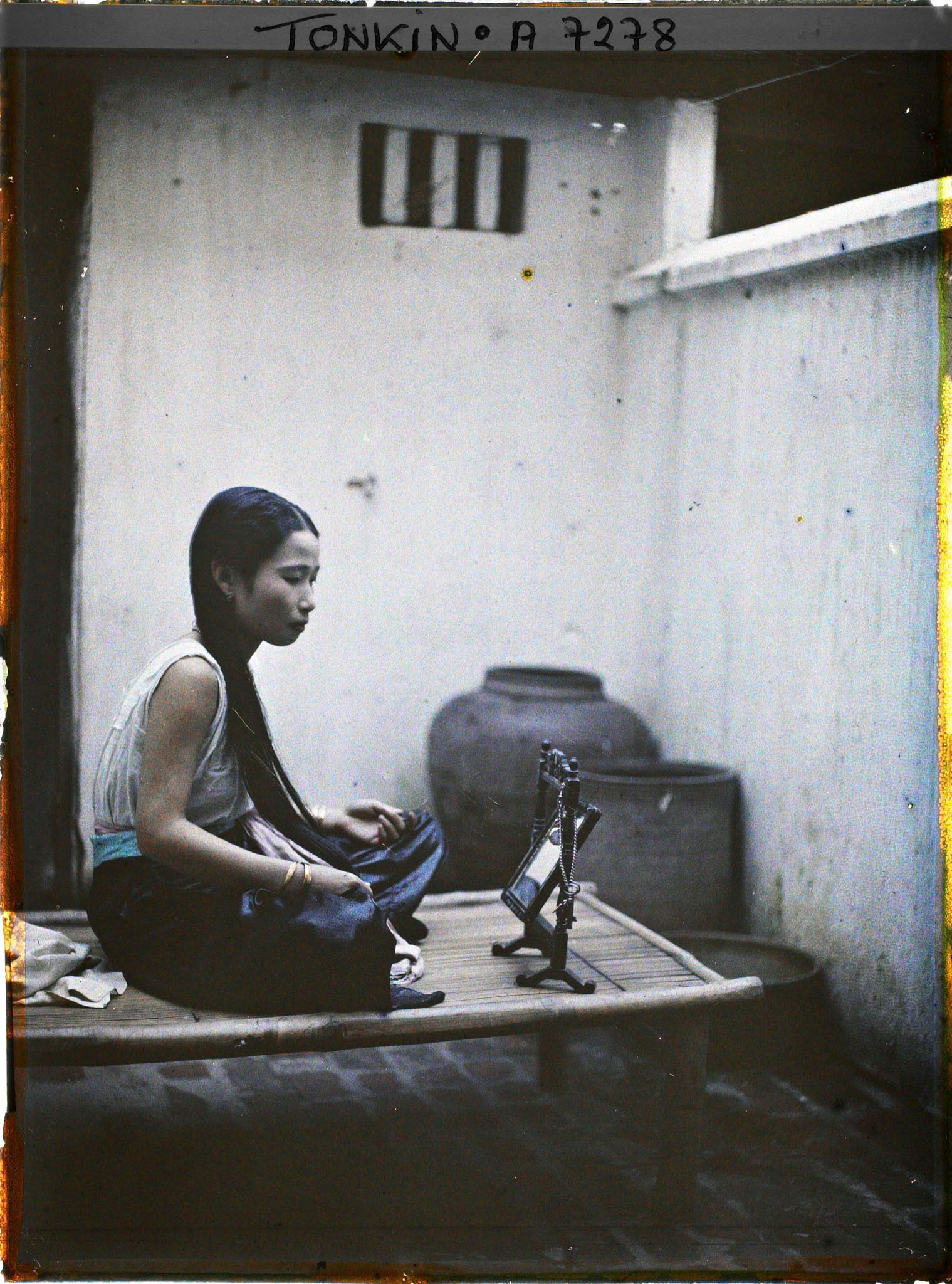 Image représentant Une jeune élégante de classe aisée à sa toilette, assise sur une banquette en bambou dans la cour intérieure de son habitation